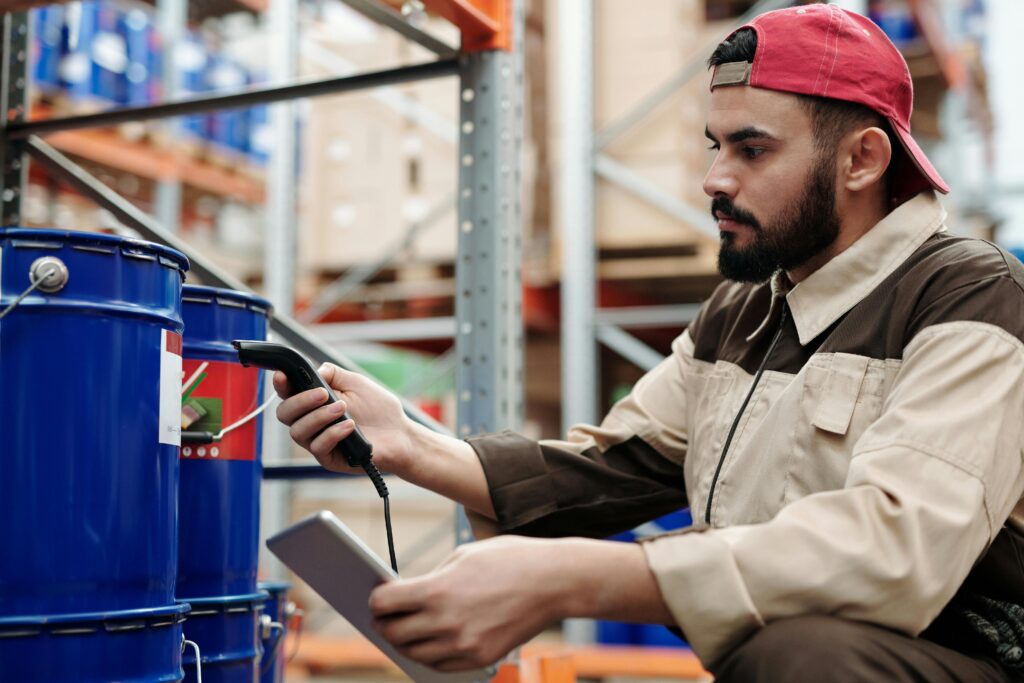 Male warehouse worker scanning barrels with a tablet for inventory management.